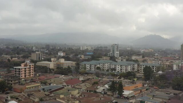 Drone video of city streets, transport, where you can see old houses, slums and the city center with skyscrapers against the backdrop of mountains in the clouds.Aerial shot of Arusha Tanzania.