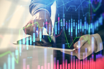 Double exposure of man's hands holding and using a digital device and forex graph drawing. Financial market concept.