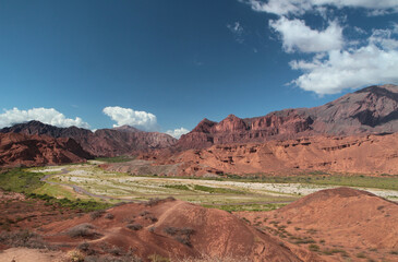 Desert landscape. Panorama view of the beautiful green valley surrounded by the red canyon, sandstone and rocky mountains under a blue sky with dramatic clouds.