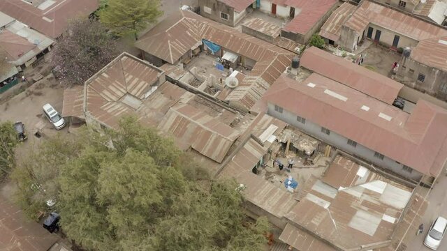 Aerial shot of Arusha Tanzania. Flying a drone over the slums in the city parallel to the houses with metal roofs through the streets with cars and trees.