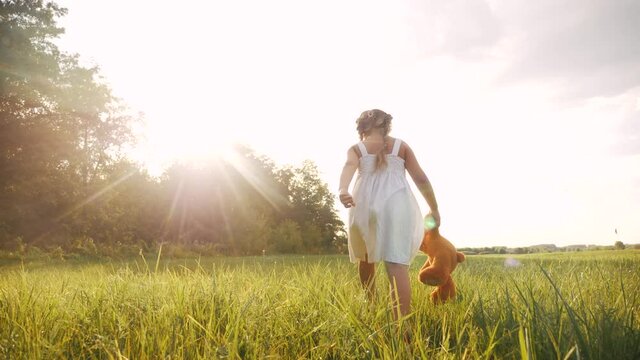 little kid girl walk with a teddy bear toy in the park in nature. childhood dream concept. smiling kid child walk with favorite toy teddy bear lifestyle dream of happiness in a green park outdoor