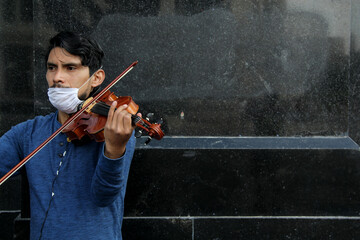 latin man with protection mask playing musical instrument violin in the street, new normal covid-19