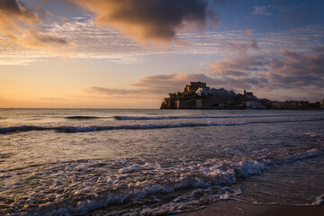 Beautiful landscape of the old town of Peniscola with the castle on the top and the sea waves on the beach in the foreground at sunrise, Pen&iacute;scola, Castellon, Spain
