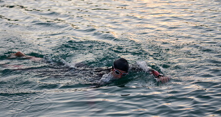 triathlon athlete swimming on lake in sunrise wearing wetsuit