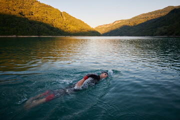 triathlon athlete swimming on lake in sunrise wearing wetsuit
