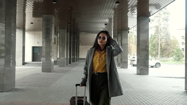 Businesswoman successful stylish young Asian woman goes from train station or airport to taxi with suitcase Luggage in Parking lot. Independent woman travels to business meetings.
