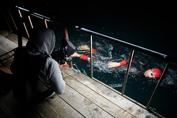 videographer taking action shot of triathlon swimming athlete at night