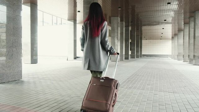 Woman comes with Luggage. Girl tourist goes on trip and walks to airport. Business successful independent woman walking down the street with Luggage in hand and exploring city.