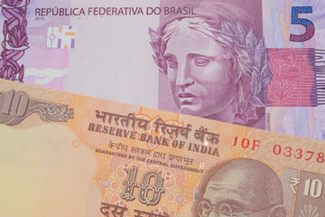 Fototapeta premium A macro image of a orange ten rupee bill from India paired up with a pink and purple five real bank note from Brazil. Shot close up in macro.