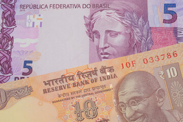 Fototapeta premium A macro image of a orange ten rupee bill from India paired up with a pink and purple five real bank note from Brazil. Shot close up in macro.