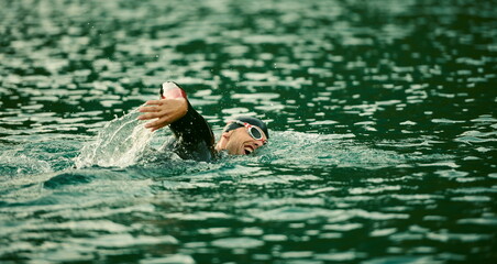 triathlon athlete swimming on lake in sunrise wearing wetsuit