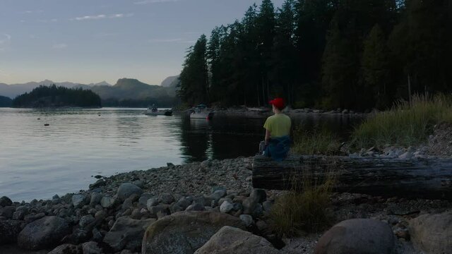 Person Sitting On A Wooden Log Watching The Sunset  From The Sechelt Inlet On The Sunshine Coast Near Egmont, British Columbia, Canada. - aerial close upshot