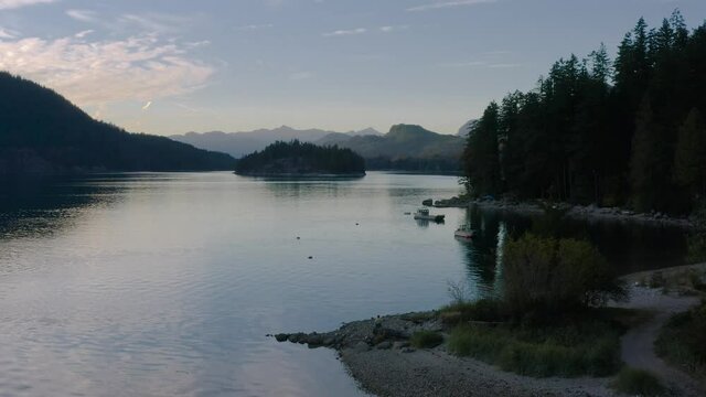 Person Sitting Watching The Calm Waters At Sechelt Inlet Surrounded By The Lush Forest On A Sunset In Sunshine Coast Near Egmont, British Columbia Canada. - aerial descending, approaching