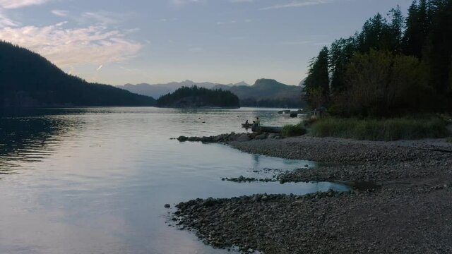 Person Sitting On A Tree Log Watching The People Boating At Sechelt Inlet On A SunSet In Sunshine Coast Near Egmont, British Columbia, Canada - drone