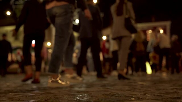 Promenade paved on stone tails full of people walking around night bars in Korca, Albania