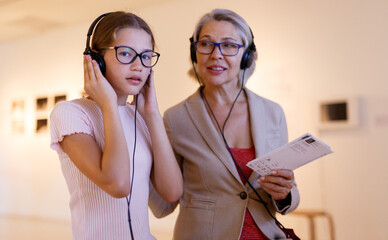Teenage girl and mature woman using audio guide during excursion in historical museum