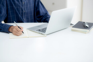 Closeup hand of business man writing on note while using laptop computer on desk at home, male planning on note for business success, author and blog, businessman working on table, employee and job.