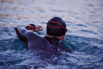 triathlon athlete swimming on lake in sunrise wearing wetsuit