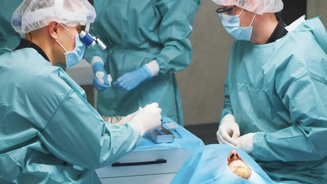 Business team of dentists and assistants cooperating in dental surgery and treating teeth of male patient. Dentistry. Surgical operation. Professionals. - Powered by Adobe