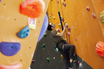 Man wearing COVID-19 or coronavirus pandemic mask climbs a wall attached to an auto belay rope in a climbing gym while following social distance guidelines