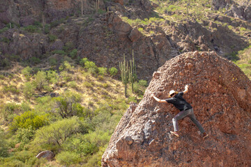 Young man boulders on a large rock in the Superstition Wilderness in the Superstition Mountains near Apache Junction, Arizona, USA in a desert environment with saguaro cactus
