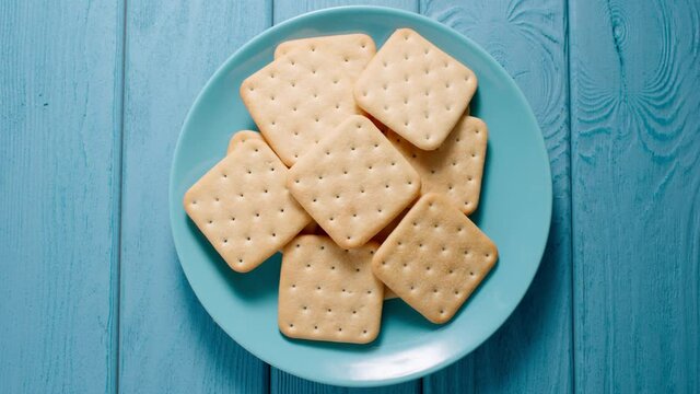 Male hands takes a cracker cookie from a plate on a blue table. Top view