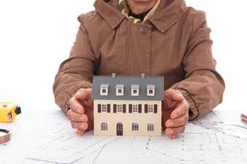 The designer cares for the small house model on the architectural drawings with both hands