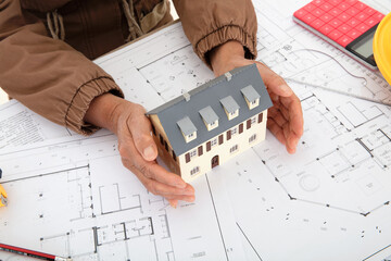 One hand holding a small house model on the drawing
