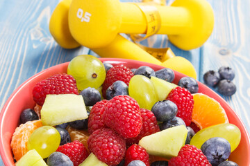 Fresh fruit salad and centimeter with dumbbells, healthy lifestyle and nutrition concept