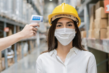 Caucasian female worker wearing medical protective mask measure temperature with thermometer infrared scan. medical healthcare for warehouse business industrial during Coronavirus pandemic