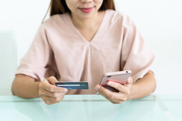 Hands of happy Asian woman using mobile phone while holding credit card in cafe. Close up. Technology and lifestyle concept.