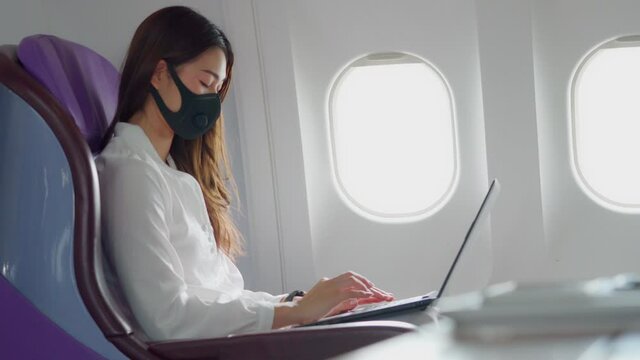 Asian young woman wearing protective mask using laptop sitting near windows at first class on airplane during flight,Traveling and Business during COVID-19 virus pandemic concept