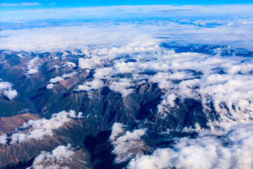 Aerial view above the clouds and mountain peaks on a sunny day.