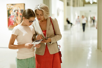 Teenage girl and mature woman observing exhibition in historical museum