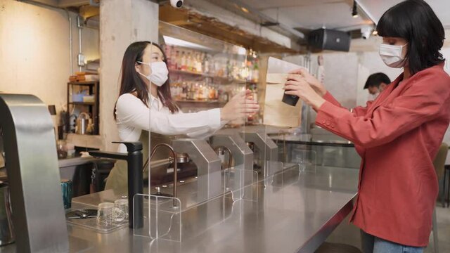 Female customer receiving food from waitress with face mask at counter