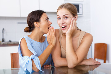 Young girl telling gossip her best friend in kitchen