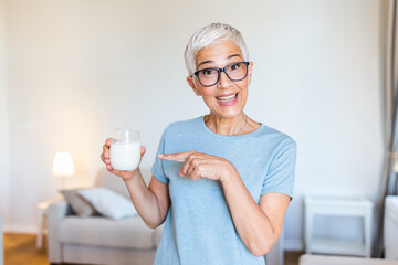 Cheerful mature woman having fun while drinking milk. Senior woman drinking from a clear glass full of milk. Woman in her golden age. Smiling, beautiful senior lady drinking a glass of milk