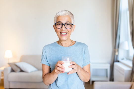 Middle age woman drinking a glass of fresh milk with a happy face standing and smiling with a confident smile showing teeth. Senior woman drinking milk at home