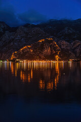 Fototapeta premium Night view of Kotor Bay with an illuminated ancient fortress city wall in the mountains, Kotor, Montenegro on the Adriatic Sea