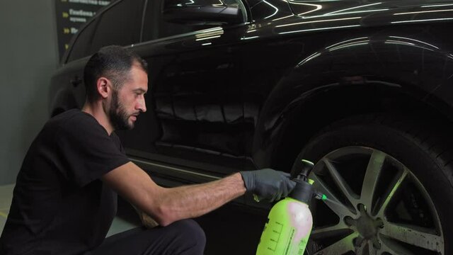 Man using chemistry for cleaning sport car wheel, slow motion. Male hand applying a special chemistry for cleaning car wheels disks via spray, close-up