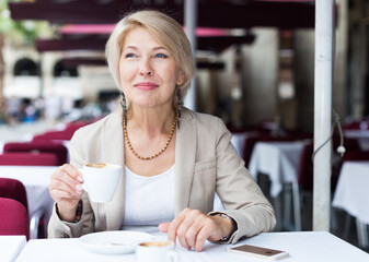 Mature businesswoman is drinking coffee in time breakfast in cafe.