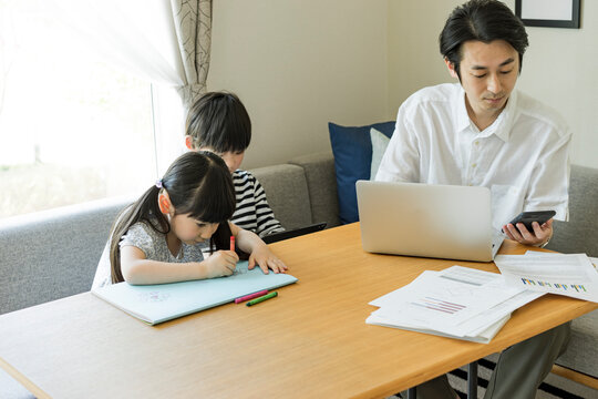 テレワークをする父親のそばで遊ぶ子供たち