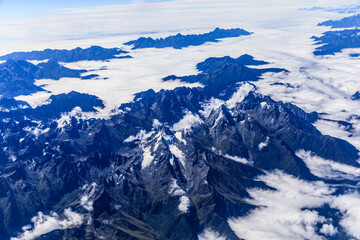 Fototapeta premium Aerial view above the clouds and mountain peaks on a sunny day.