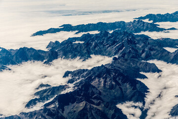 Aerial view above the clouds and mountain peaks on a sunny day.