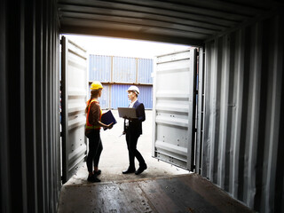 Young Engineers standing in the shipping yard tracking the cargo inventory and checking container box for safety.