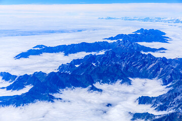 Aerial view above the clouds and mountain peaks on a sunny day.