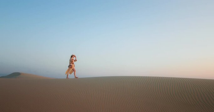 Cinematic footage with copy space on light blue background in soft sunset light. Scenic landscape view with plain nature background for commercial text. Woman walking by sand dune and desert scenery