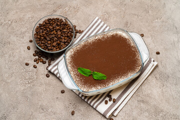 Traditional Italian Tiramisu dessert in glass baking dish on concrete background