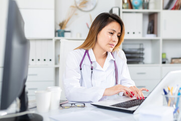 Woman doctor in uniform is working behind laptop in clinic