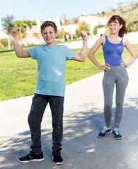 Happy friendly family of mother and preteen son wearing sports clothes ready for workout outdoors